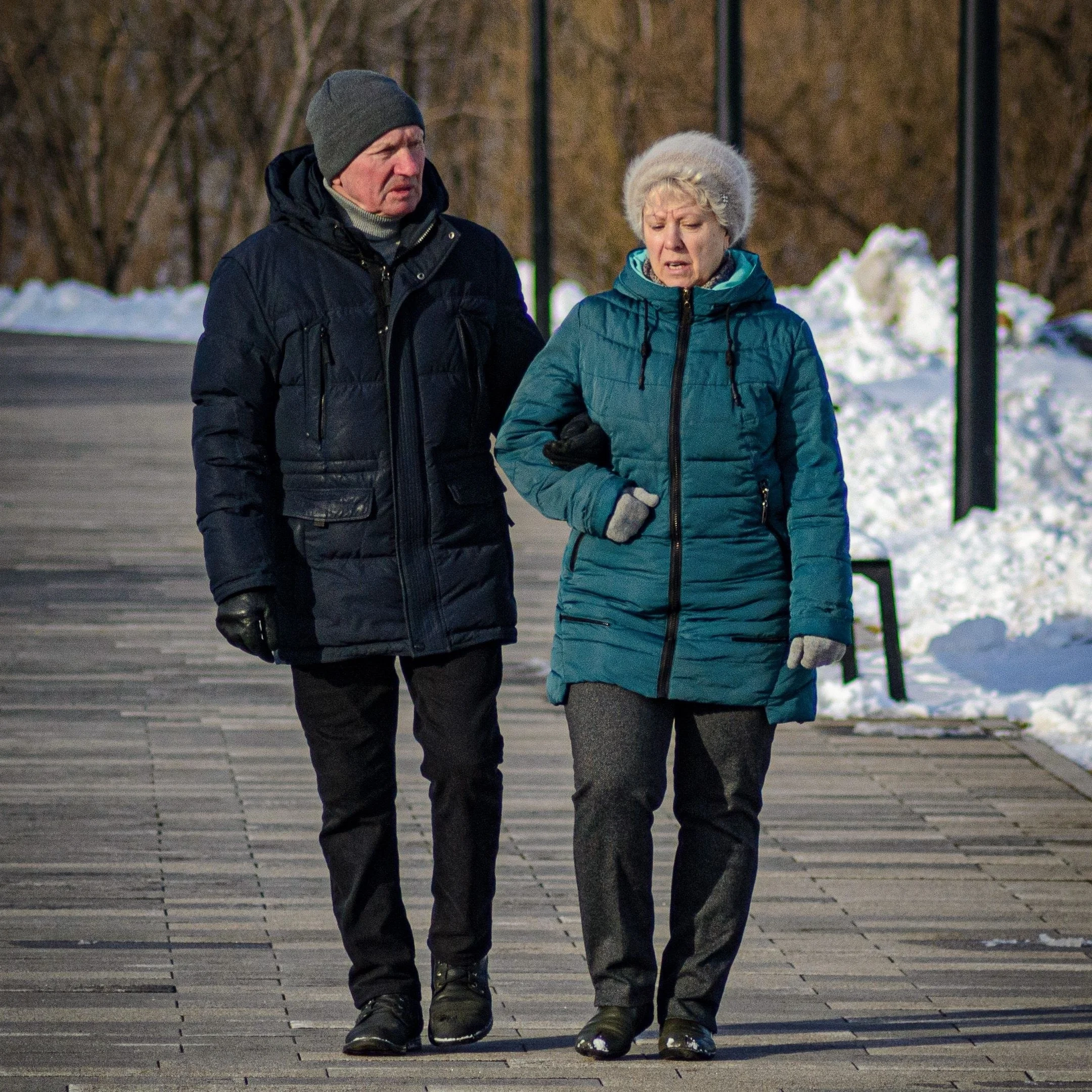 Casal de idosos agasalhados, de braços dados, caminhando ao ar livre num dia frio
