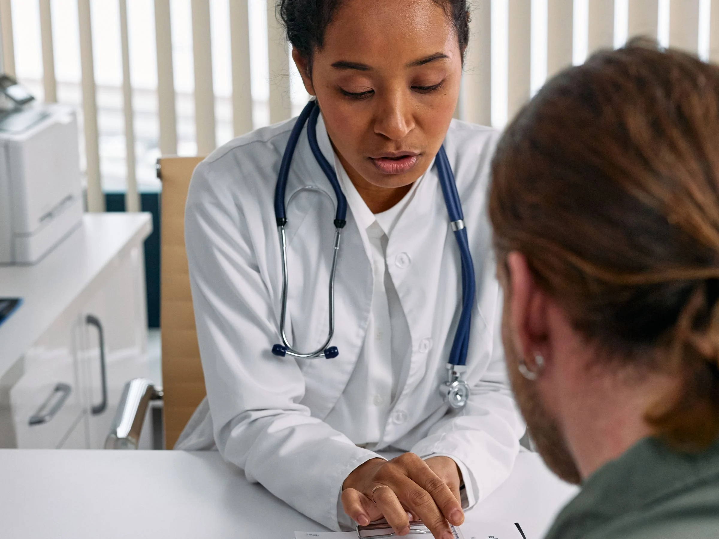 Médica conversando com uma paciente do outro lado da mesa, com exames à frente