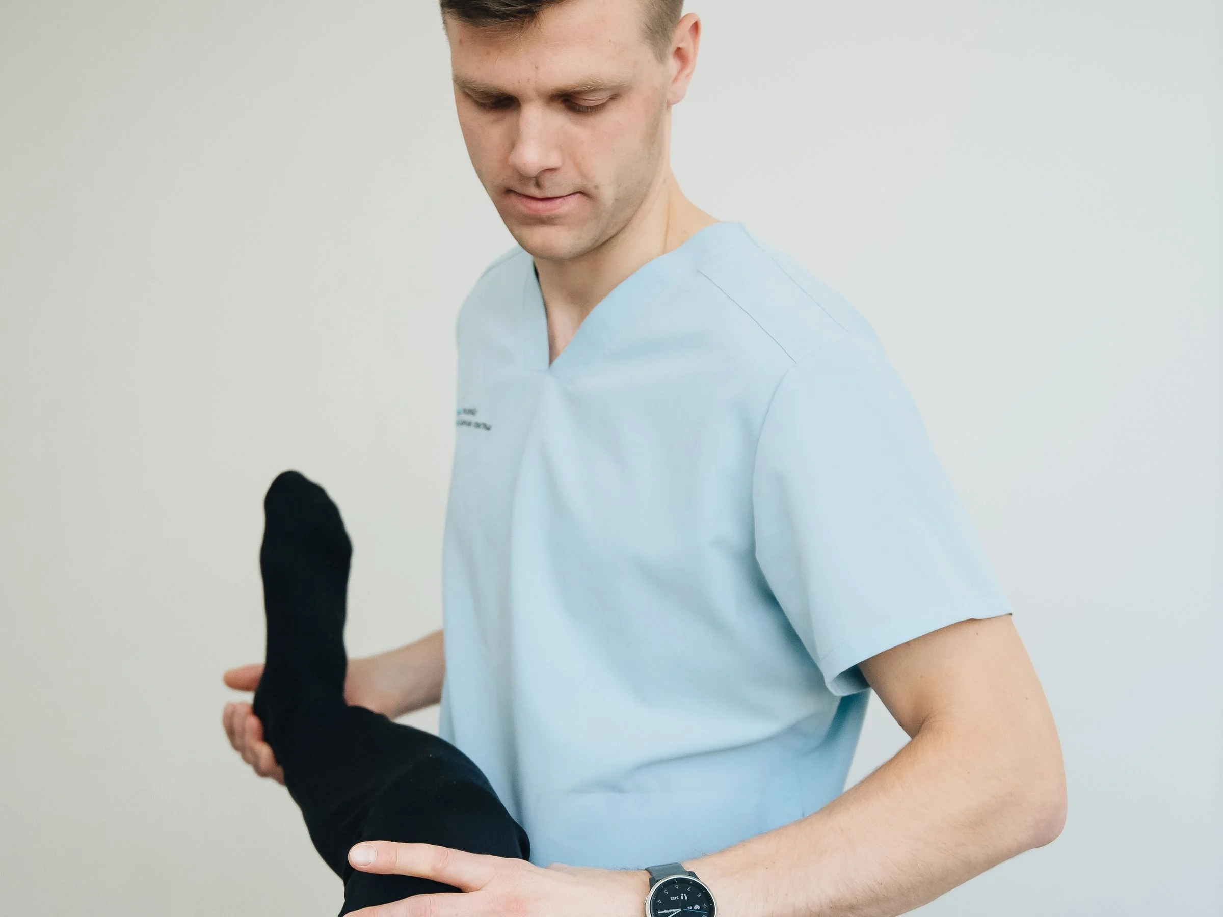 Fisioterapeuta de uniforme mobilizando o joelho de um paciente deitado na maca, apoiando a perna com as duas mãos